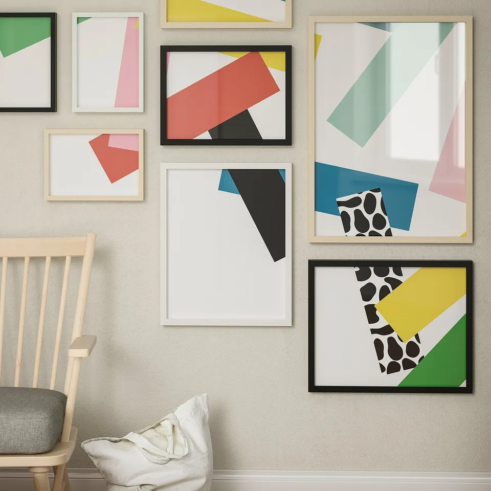 Abstract art prints in black, white, gold, and wood frames on beige wall. Chair with grey cushion left.