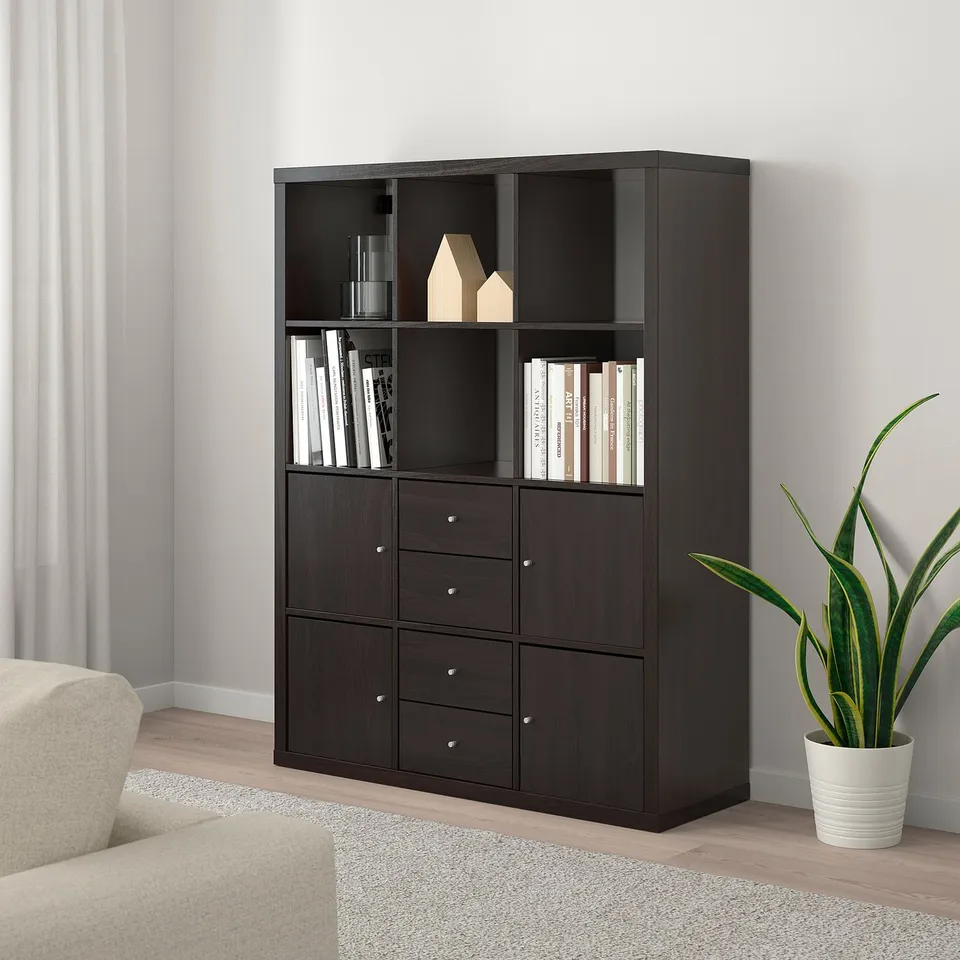 Large KALLAX black storage unit in modern room with shelves and drawers holding books and decor. Positioned near light-colored sofa and potted plant.