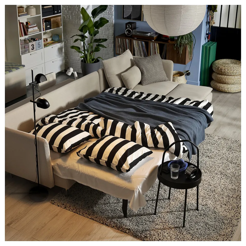 Cosy living room with SÖDERHAMN sofa-bed, striped black-and-white pillows, blue blanket, wooden floor, and brick wall.