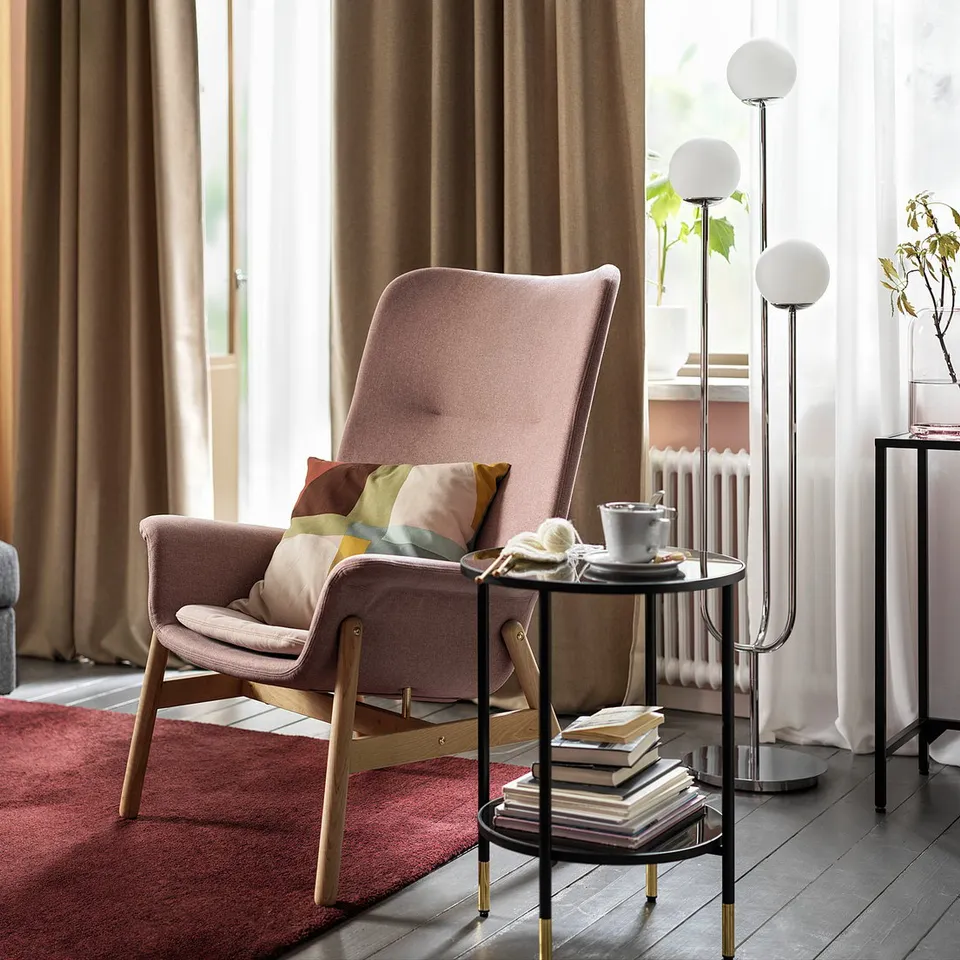 Modern living room with VEDBO armchair in brown-pink, plush cushions, side tables, grey sofa, bookshelf, and large window with curtains.