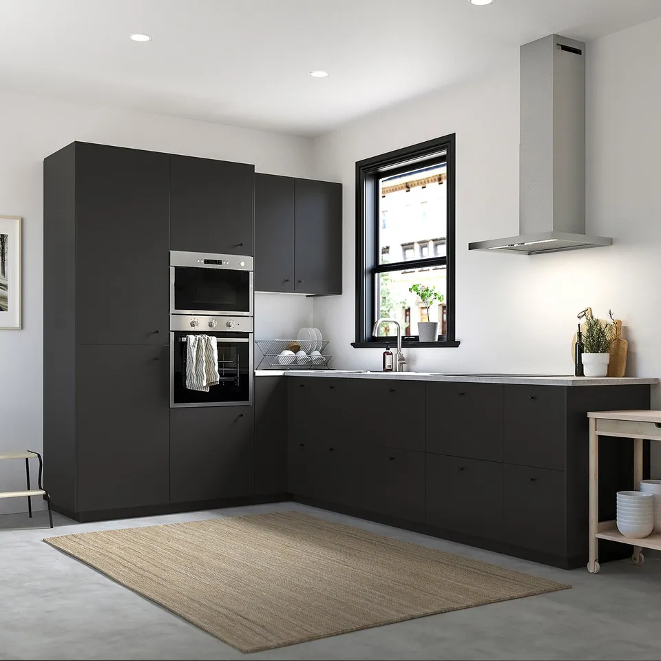 Modern kitchen with black NICKEBO cabinets, sleek oven, and plants by window. Cabinets are large, reaching high ceilings.