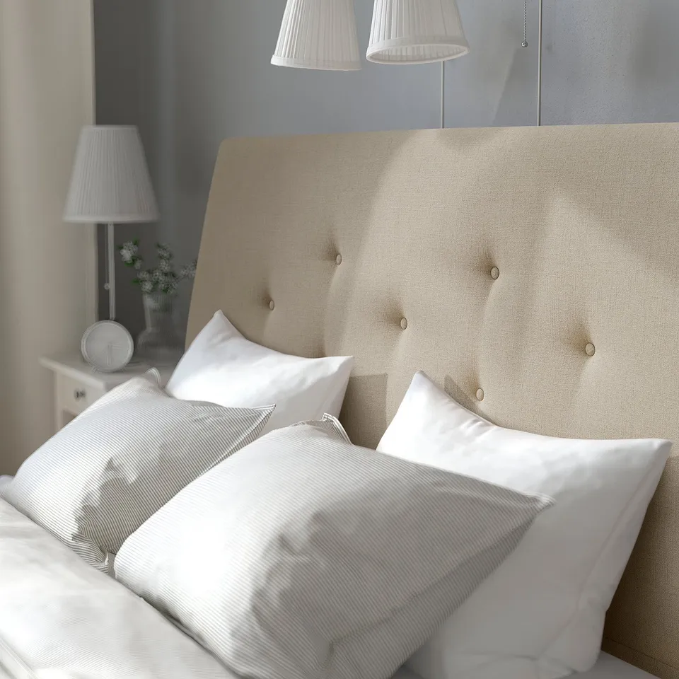 Beige tufted headboard with white bedding, lamps, and floral vase.