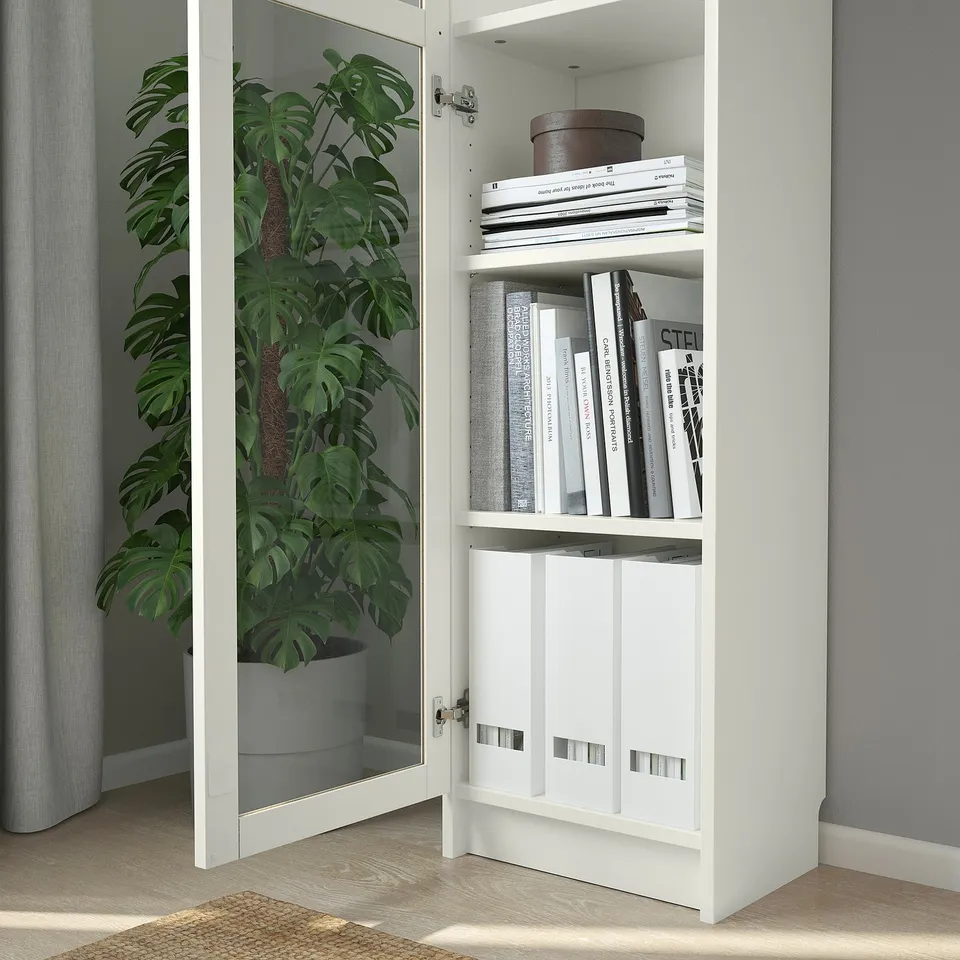 White BILLY bookcase with glass doors displays various books and a potted plant inside, utilising vertical space efficiently.