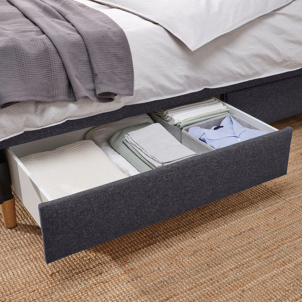 Under-bed drawer open, showing neatly folded linens. Drawers provide under-bed storage for sheets and bedding.