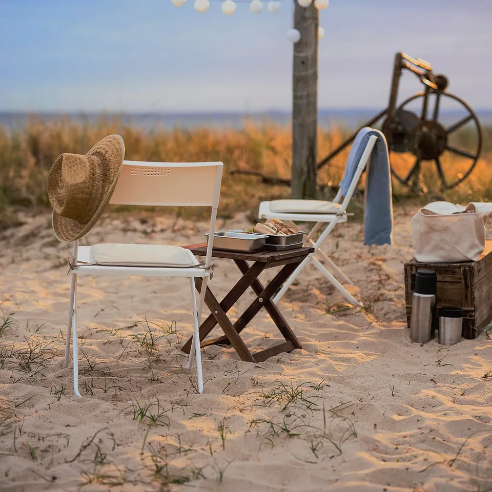 Cosy beach setup: pink FEJAN folding chairs, hat, and string lights on sand.