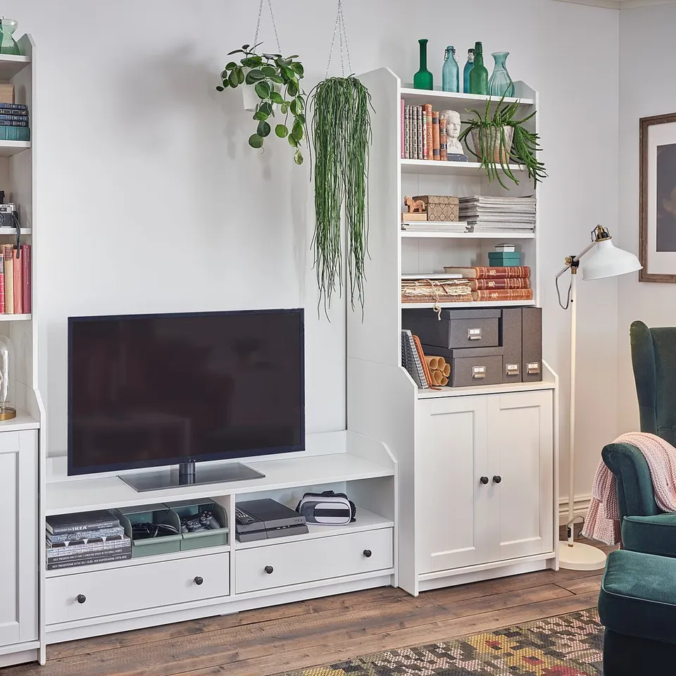 Stylish living room setup with white HAUGA tv unit and bookshelves, featuring a flat screen tv, decorative items, books, and plants.