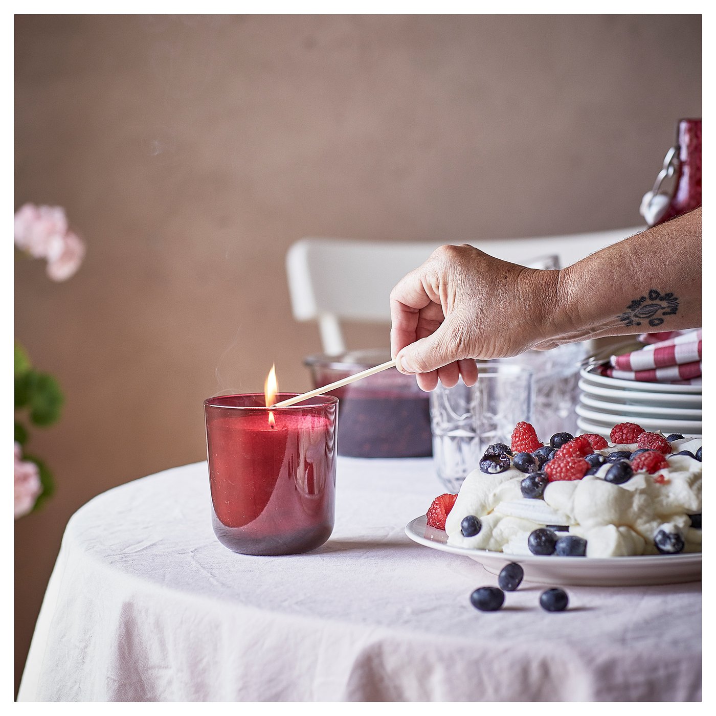 A hand lights a red STÖRTSKÖN candle on a table set with a cream berry dessert and a white tablecloth.