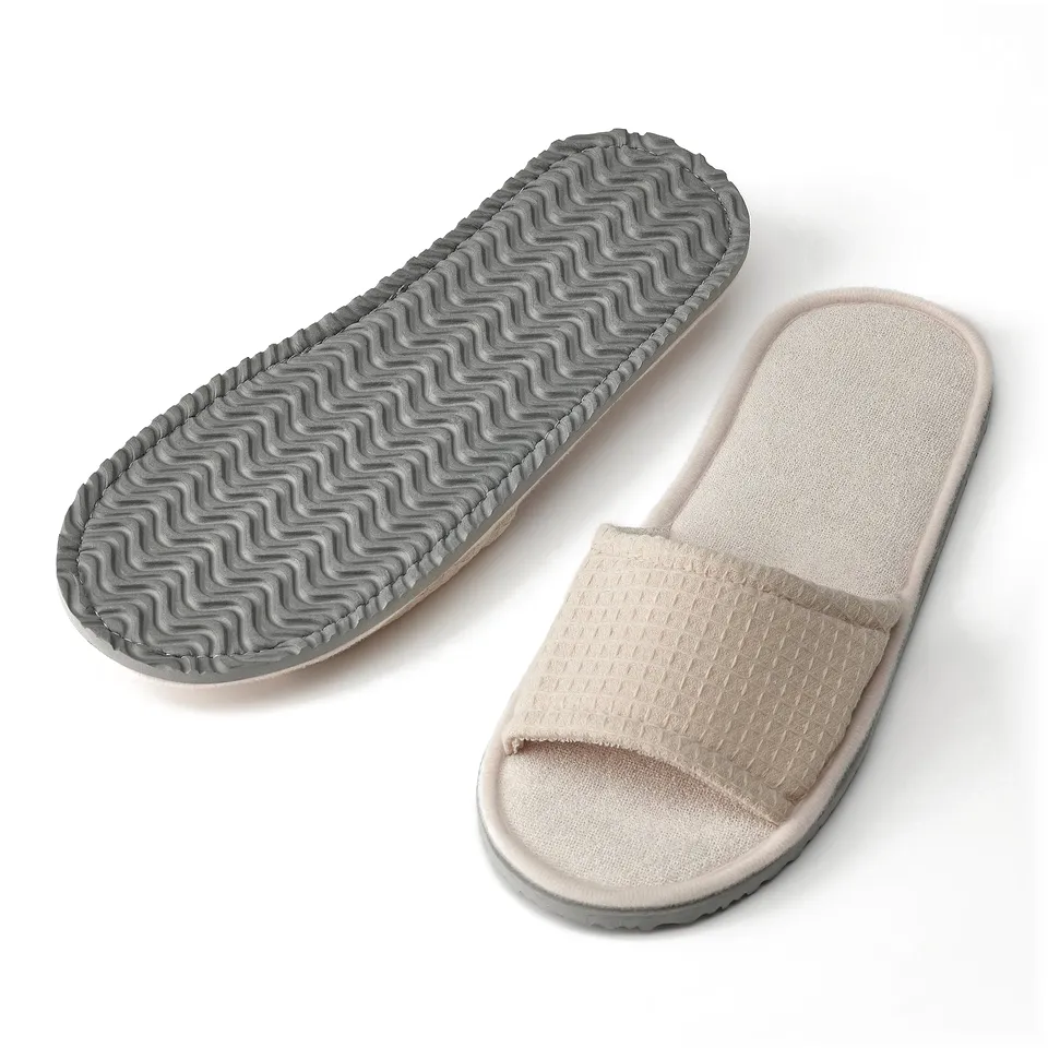 Two beige slippers with waffle-textured soles for comfort. One shown from top, one from side, highlighting cushioned foam soles.