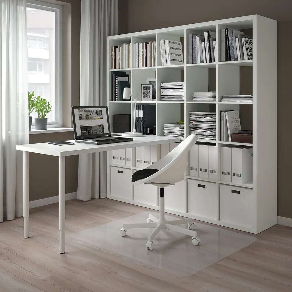 Modern home office with white INLÄGG desk, chair, kallax shelf with books, laptop, and lamp. Compact but functional setup.