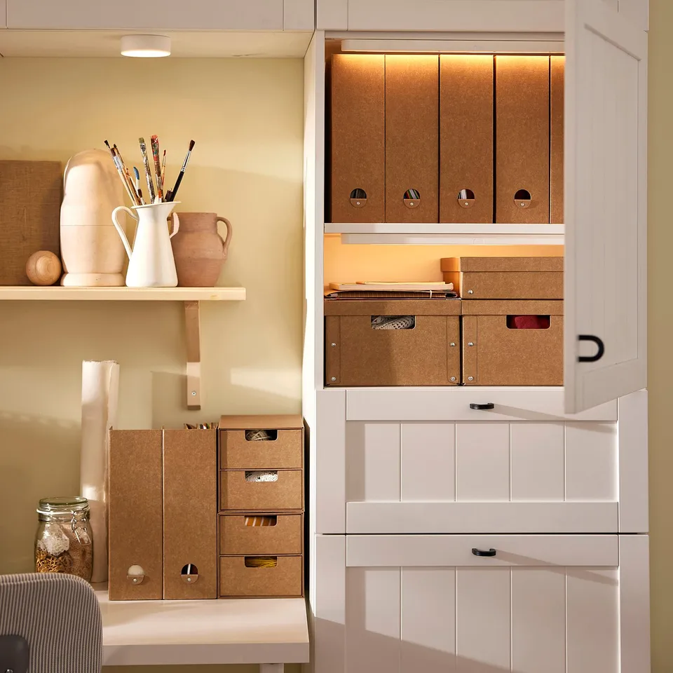 Organised office setup with beige GÄRDESGÅRD files made of recycled paperboard, stored in white cabinets, holding various office supplies.