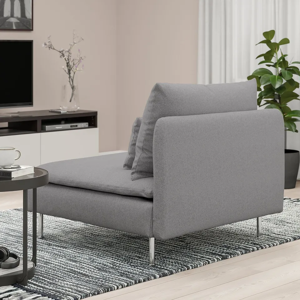 A grey fabric chaise lounge with a grey pillow on a patterned rug in a modern living room.