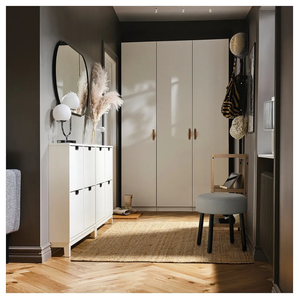 Modern entryway with white MÖRTFORS shoe cabinet, tall white wardrobe, round mirror, grey stool, jute rug, and coats on rack.