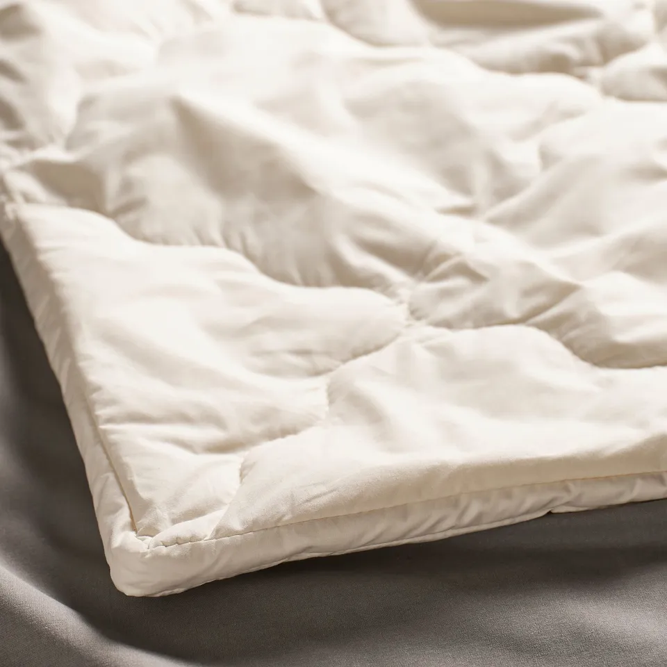 Close-up of luxurious, cream-colored, quilted bed cover made of premium, soft fabric with even stitching, showcasing high quality.