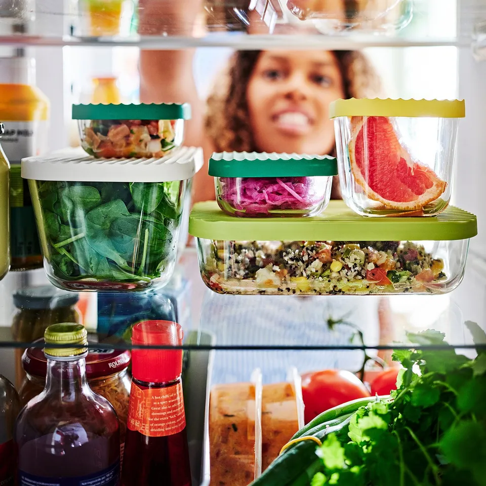 Fridge with HAVSTOBIS glass containers in green, yellow, white, holding spinach, onions, citrus, mixed dishes.