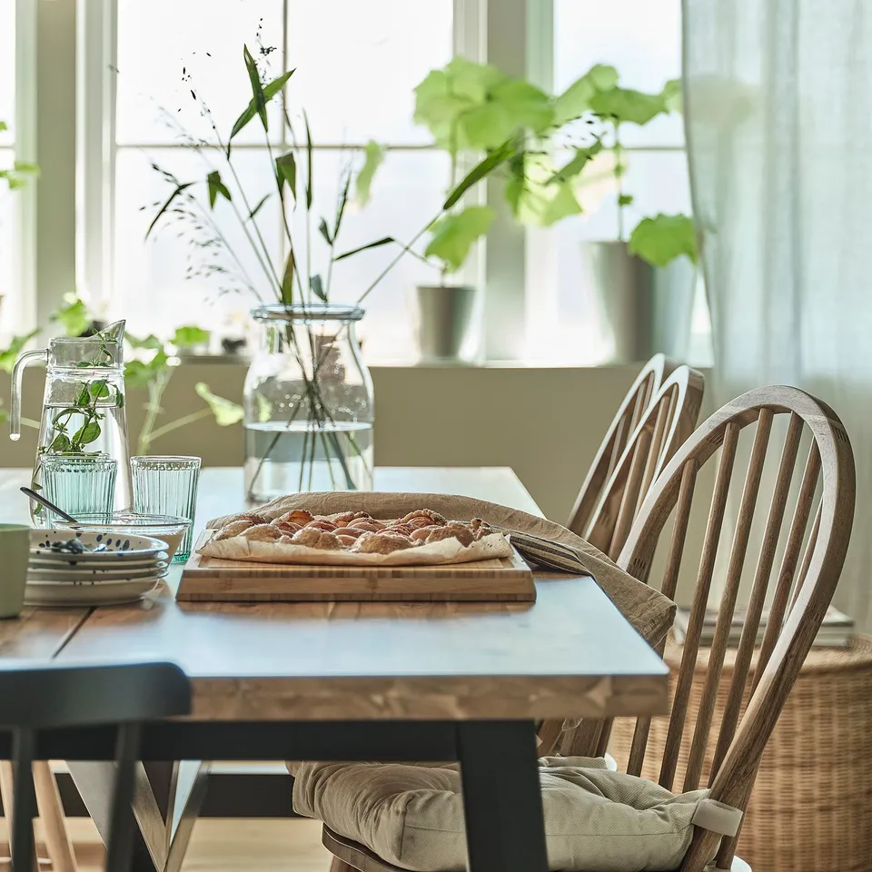 SKOGSTA chair in brown wood near dining table with food, vase, and glasses.
