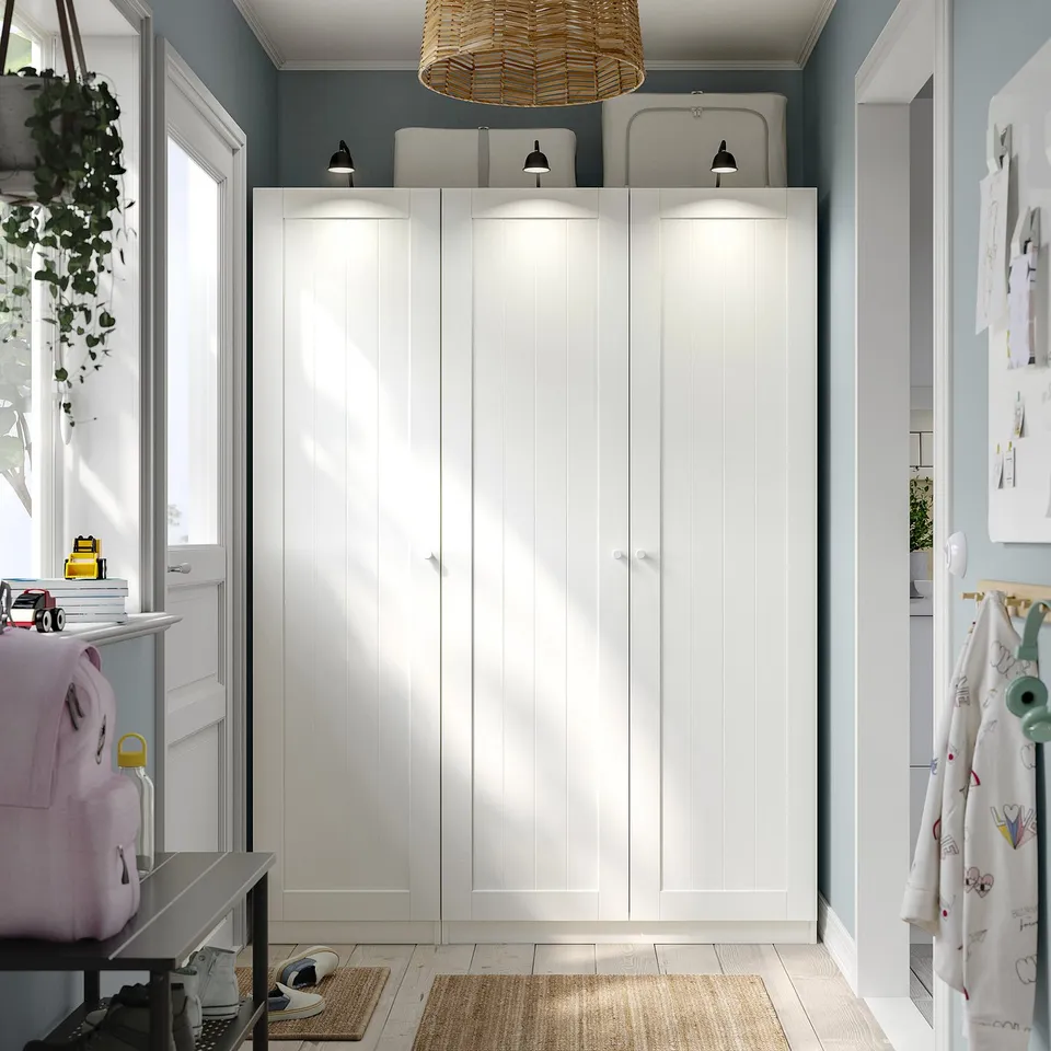White PAX wardrobe in room corner with pendant light, table, toys, plants.