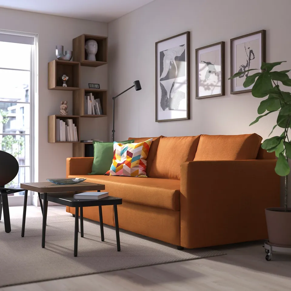 Bright orange FRIHETEN sofa, modern and colourful, with storage. -positioned near window, shelves, & plant.