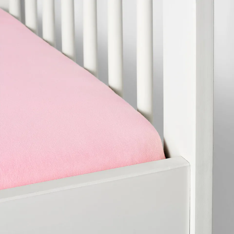 Close-up of a pink fitted crib sheet with white vertical bars, showcasing its elastic corner designed to stay secure on a mattress.