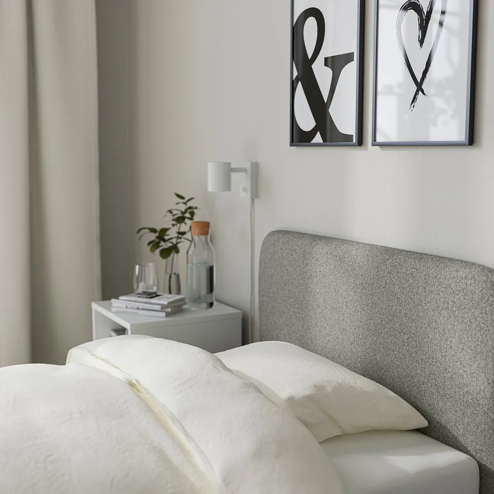 Modern bedroom with light bedding on SLATTUM bed, padded headboard, plant, and artwork.