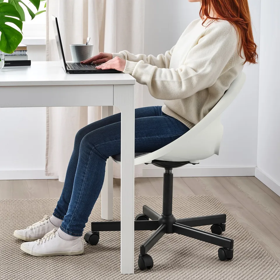 Person sitting in a white office chair, typing on a laptop at a white desk.