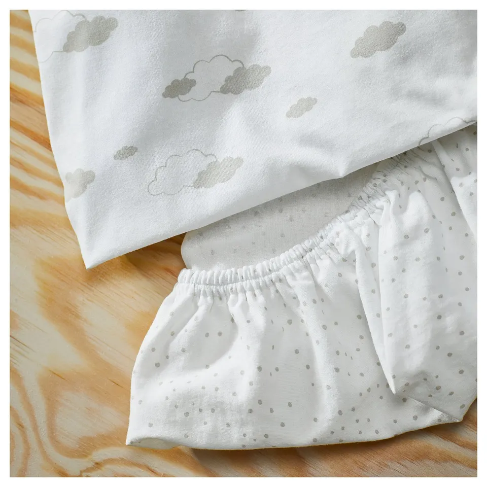 Image shows white baby clothing with cloud and dot patterns, laid on a wooden surface.