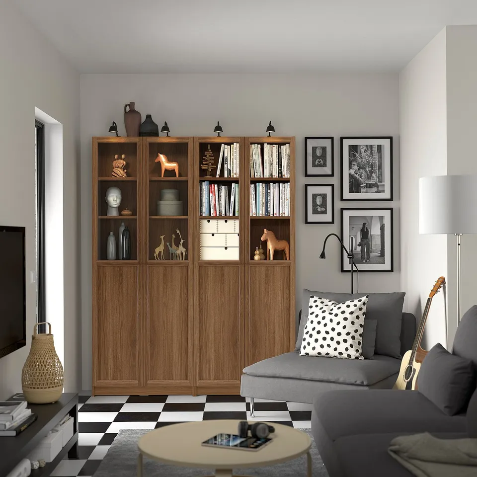 Modern living room with large BILLY brown wood bookshelf, grey couch, black & white decor, and guitar.