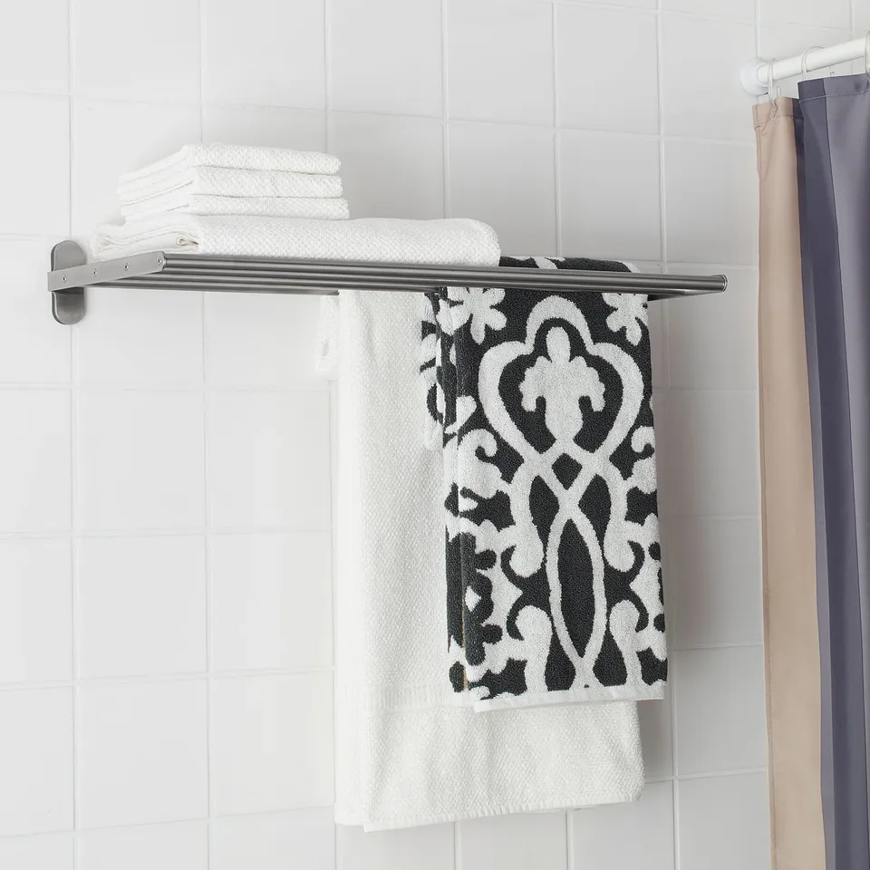 A silver wall-mounted towel rail with a shelf holds stacked white towels and a black and white patterned towel beneath.