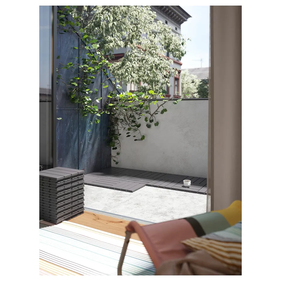 View from a window to a balcony with RUNNEN grey floor decking and a green plant on a wooden wall.