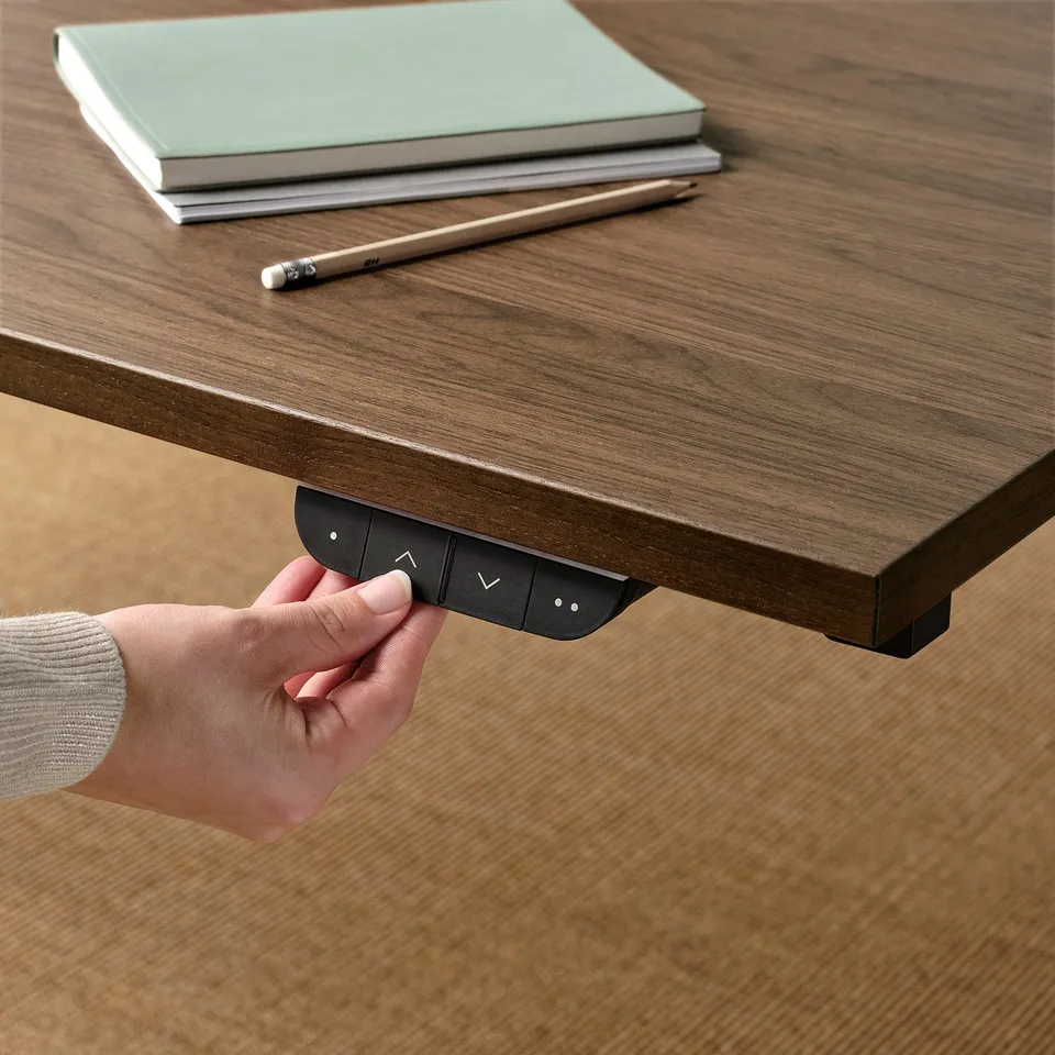Person adjusting height of MITTZON sit/stand desk with hand control, improving ergonomics.
