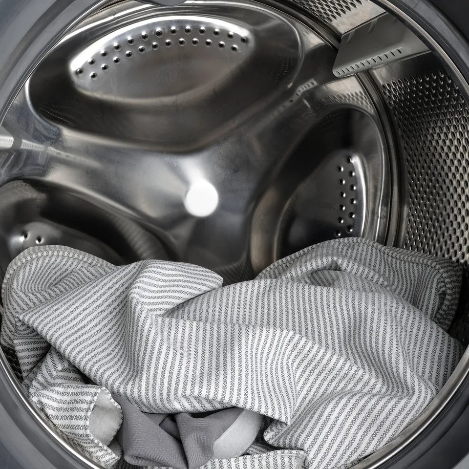 A stainless steel washing machine with a striped shirt inside; machine washable and removable bed cover.