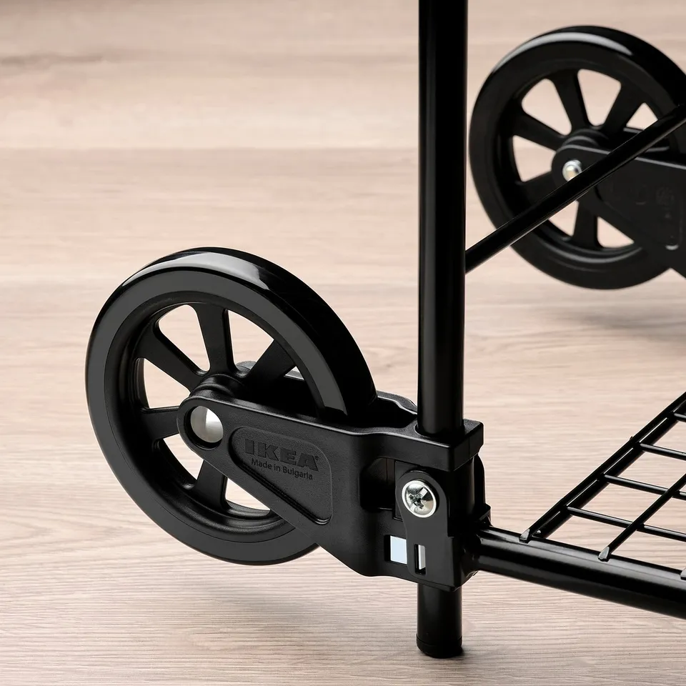 Black trolley wheel detail, showing brand ikea on metal frame, on wooden floor.