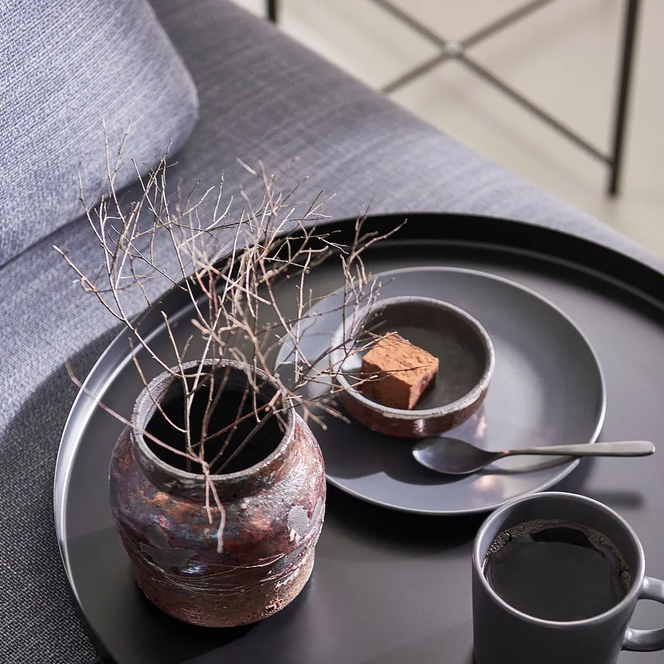 Black tray with handle, holding coffee cup, bowl, spoon, and rustic vase with branches.