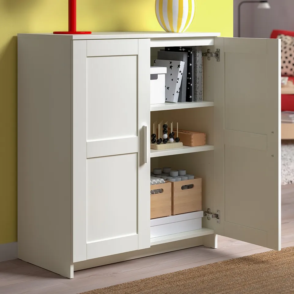 White wooden cabinet with one door open, revealing an organised interior with shelves holding wooden boxes and other items.