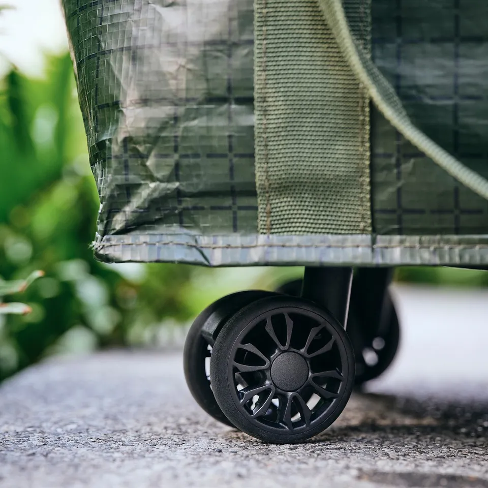 Close-up of a sturdy shopping bag with robust black wheels and a strong mesh material, ideal for carrying items effortlessly.