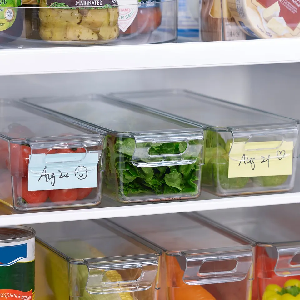 Clear fridge storage boxes with lids, labels, and handles, organising vegetables and fruits in a well-structured fridge.