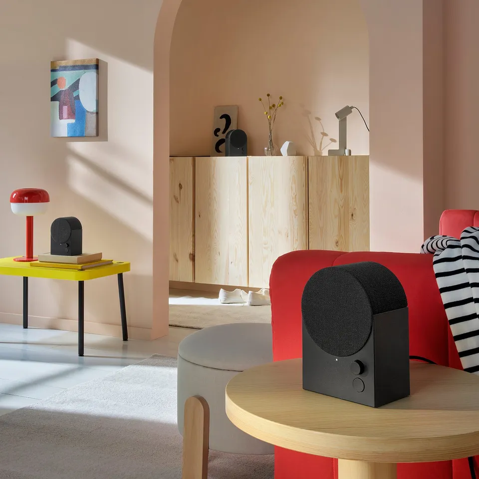 Modern living room with NATTBAD bluetooth speaker on table, red lamp, colourful decor, and wooden furniture.