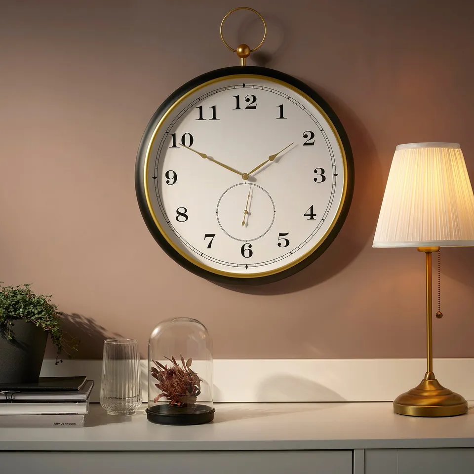 Large round wall clock, styled like an old pocket watch with black face and gold accents, mounted above a shelf.