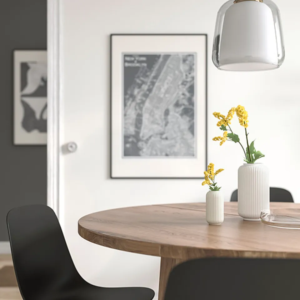 Minimalist dining area with wooden table, black chairs, two STILREN vases with yellow flowers, pendant lamp, and framed art.