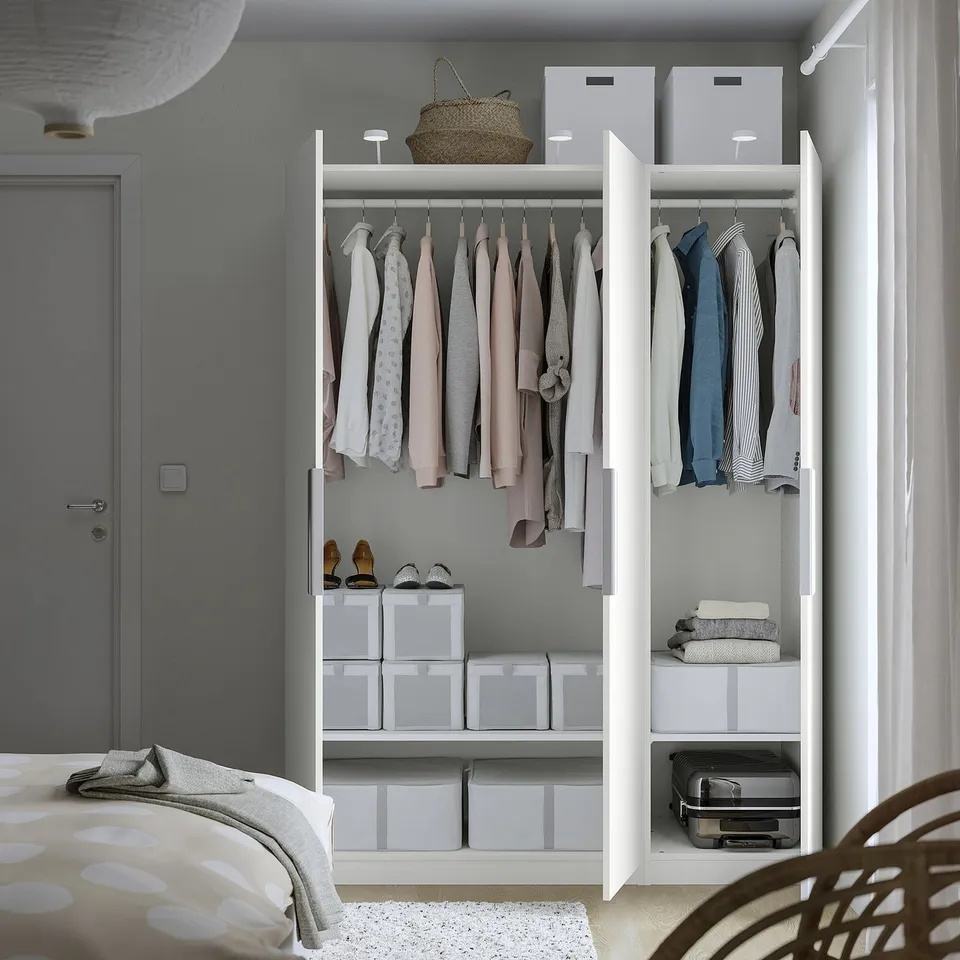 Open closet displaying clothes and storage boxes, organised with white shelves and hanging rods.