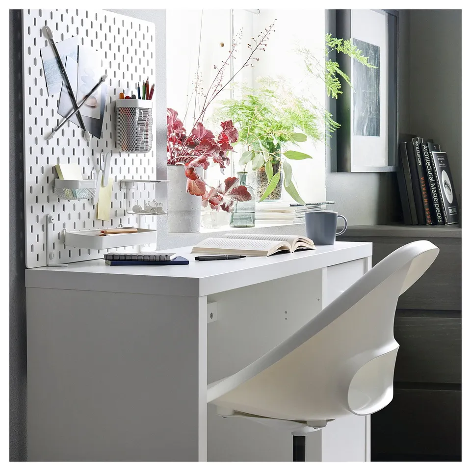 Modern white workspace with pegboard, plants, and minimalist desk and chair.