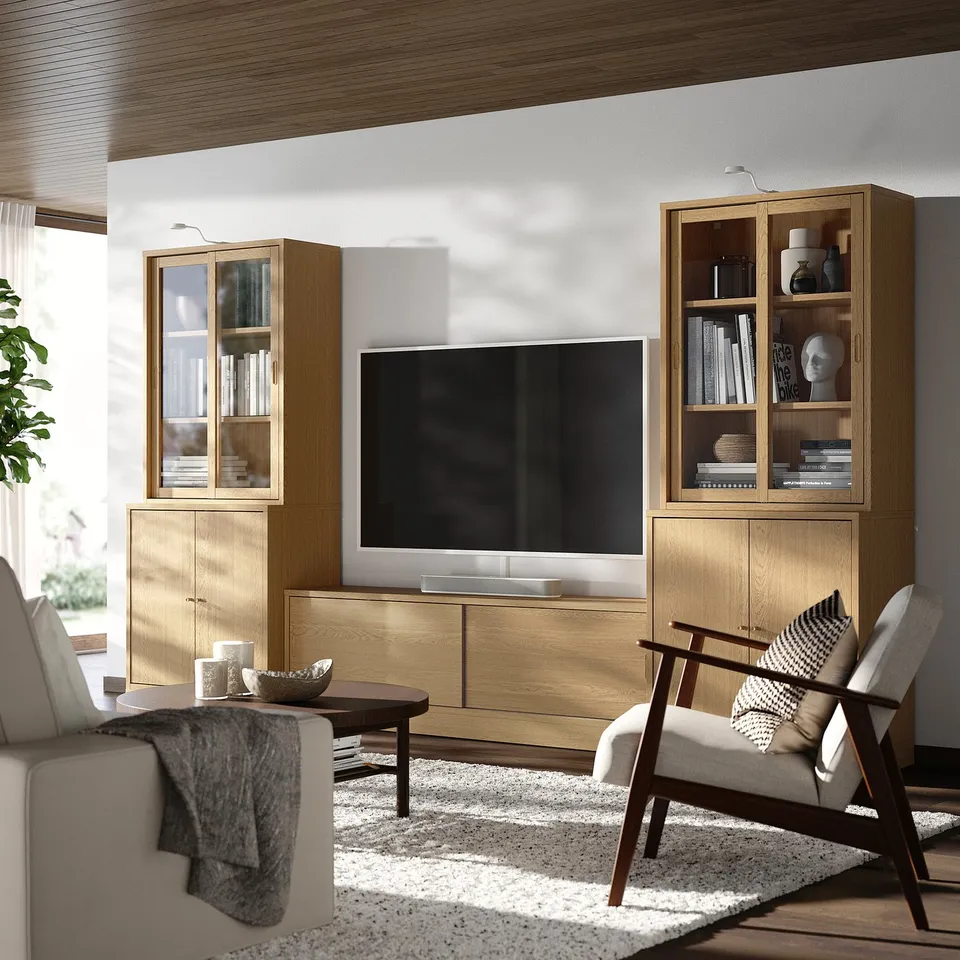 Modern living room with oak tv unit, large tv, two armchairs, and rug. Decor on shelves, nature light from window.