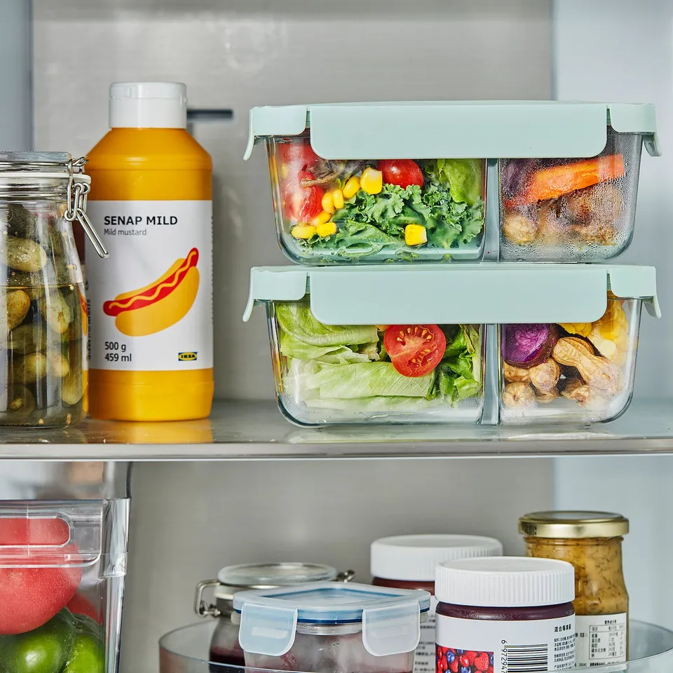 Fridge shelf with glass HAVSTOBIS lunch boxes, storing vegetables separately in compartments. Next to yellow mustard bottle labelled senap mild.
