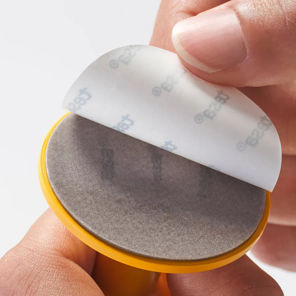A hand peels label off yellow hook, revealing textured surface.