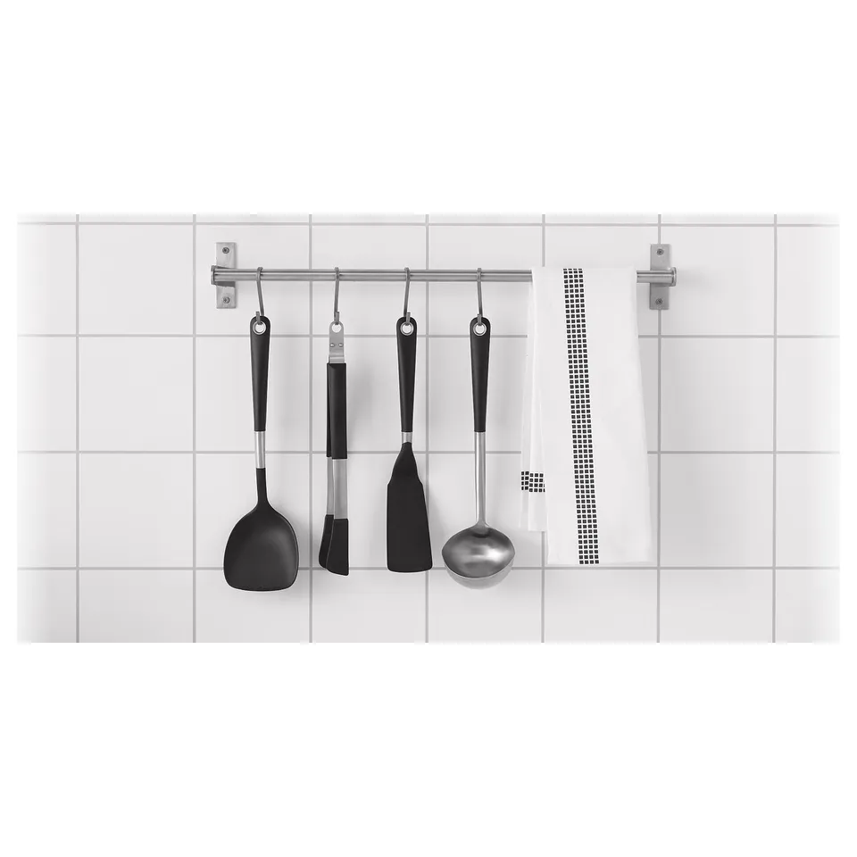 Four black kitchen utensils hang on a metallic rod against white tiles.