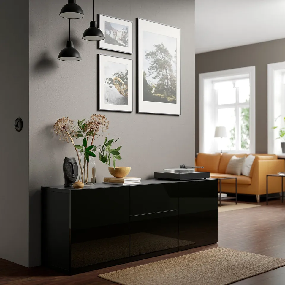 Stylish black storage cabinet, modern design, gloss finish, positioned under large framed art, holding plants, books.