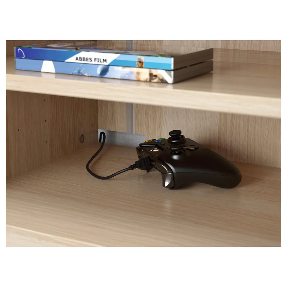 Black gaming controller resting on wooden shelf, plugged into cable outlet.