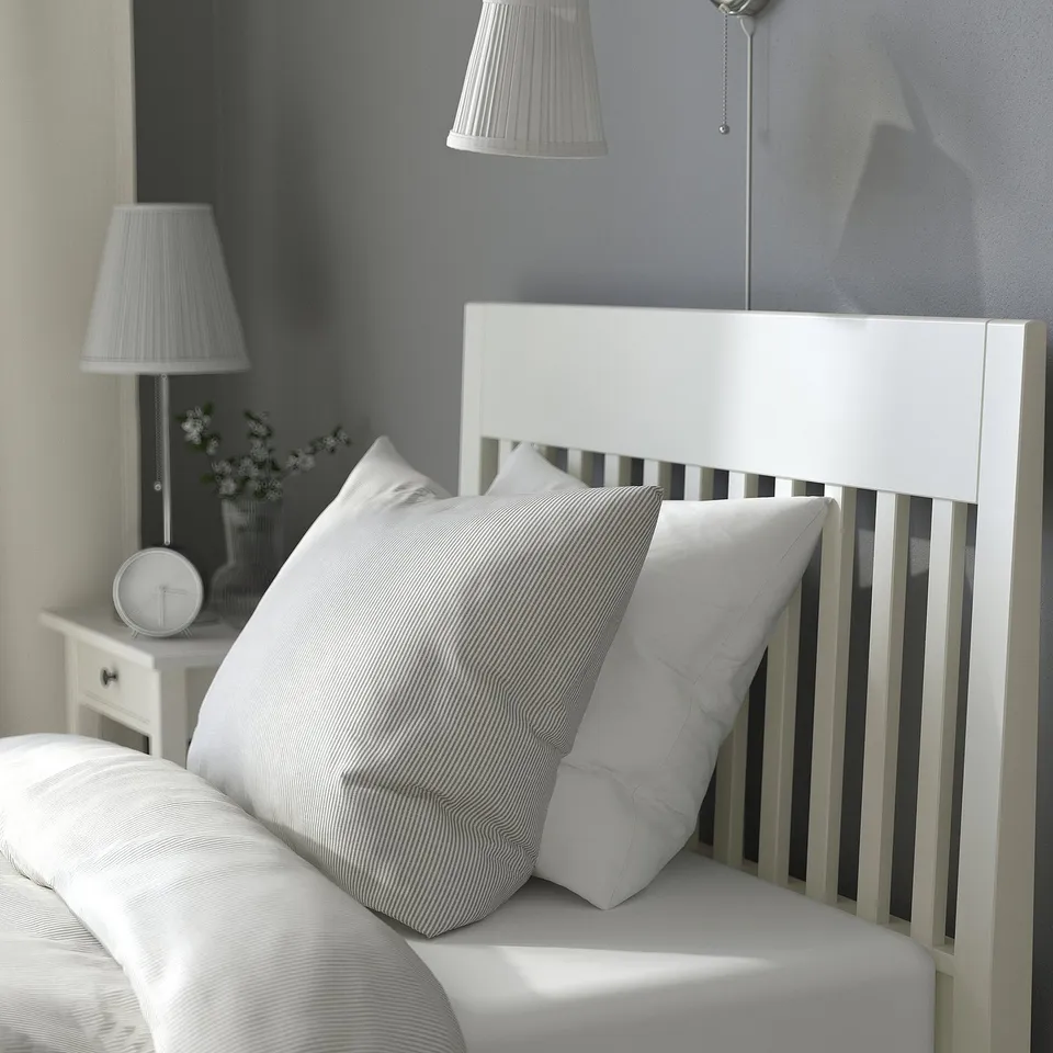 Bedroom scene featuring white IDANÄS bed with striped pillows, headboard, and bedside table with lamp.