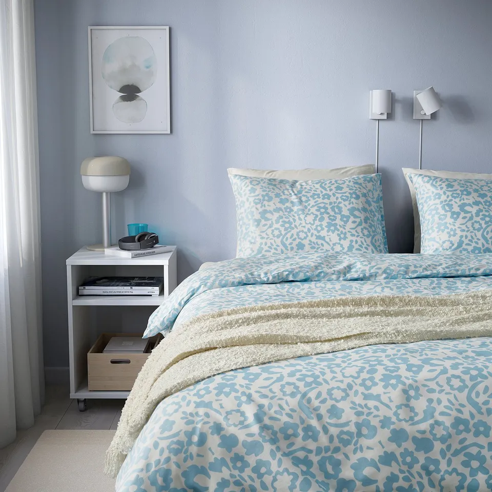 Modern blue floral bedding set on twin bed, with two wall lamps.