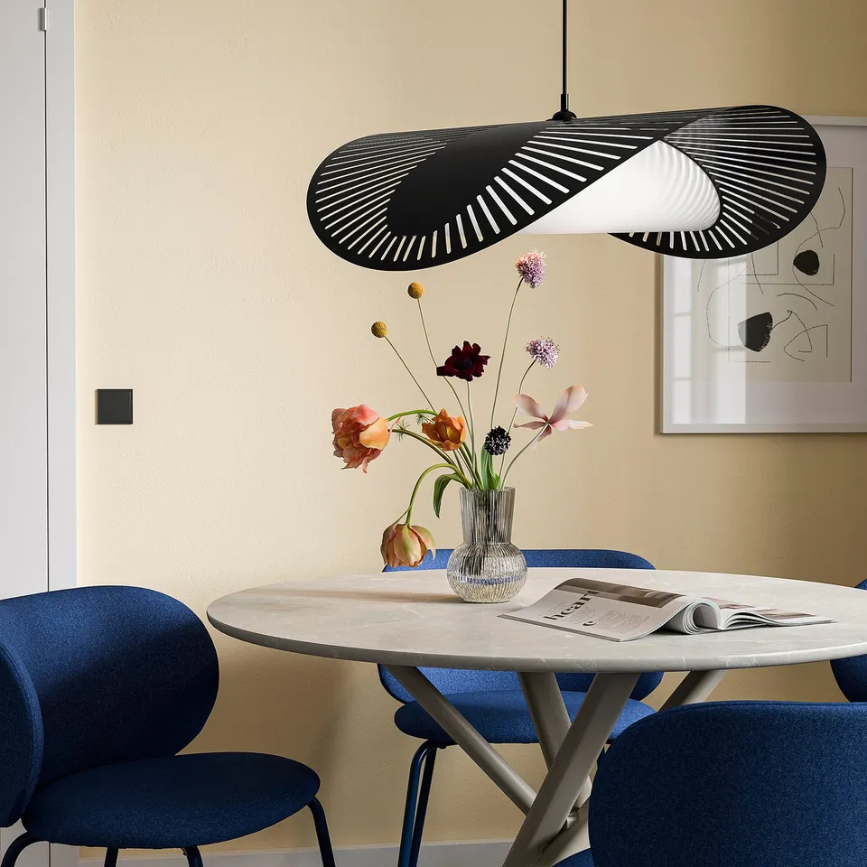 Modern dining area with KVÄLLSDOPP black pendant lamp, blue chairs, marble table, and floral vase, set against a beige wall with art.