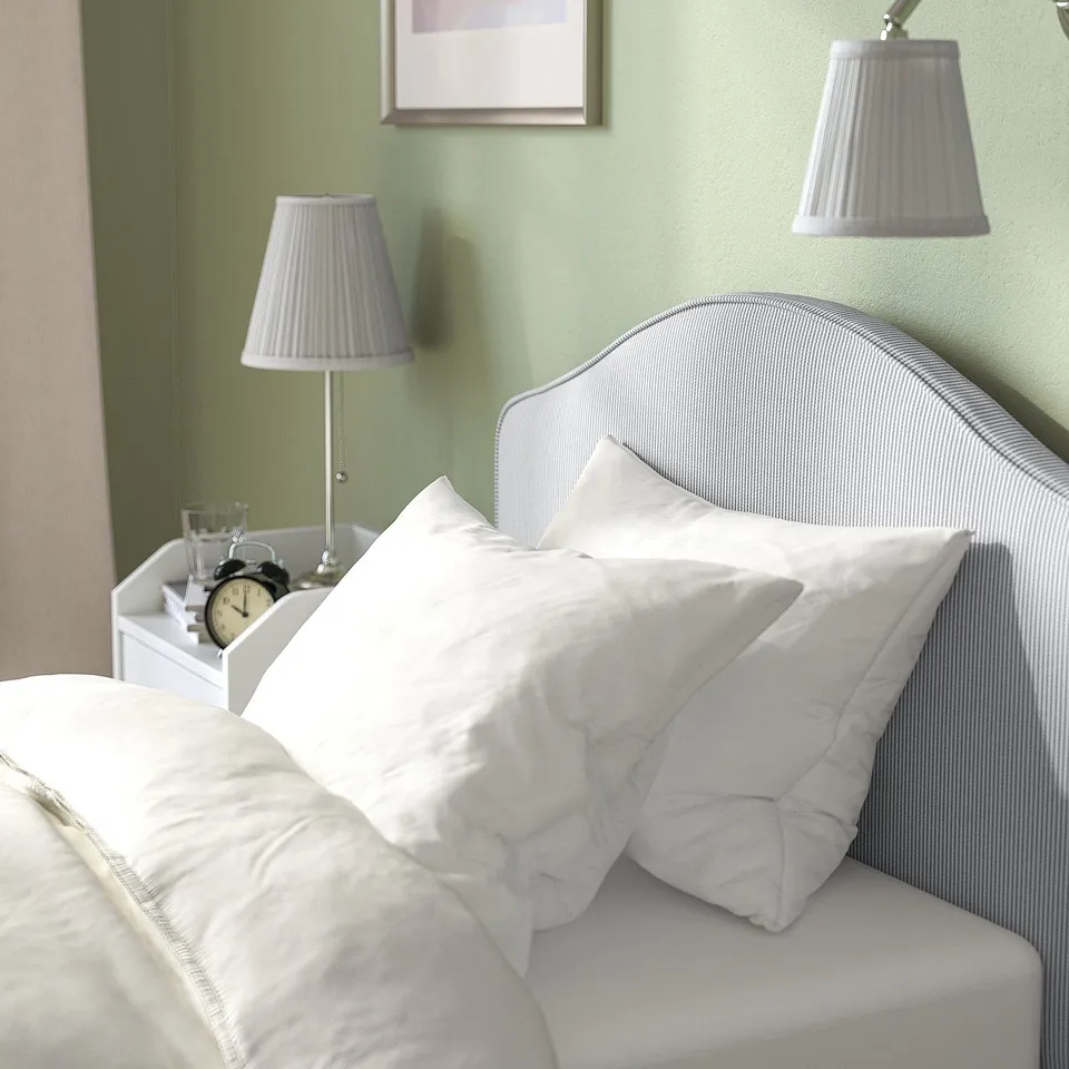 Cosy bed with soft, washable headboard; includes lamps, clock, and glass on bedside table.